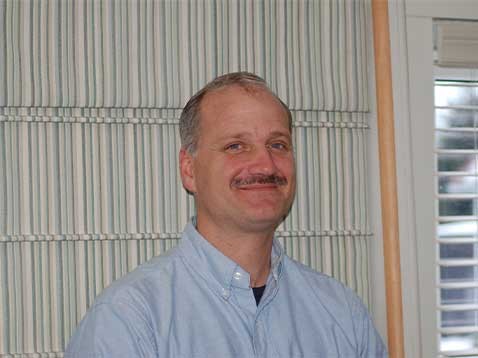 Portrait of a man with a mustache wearing a blue collared shirt