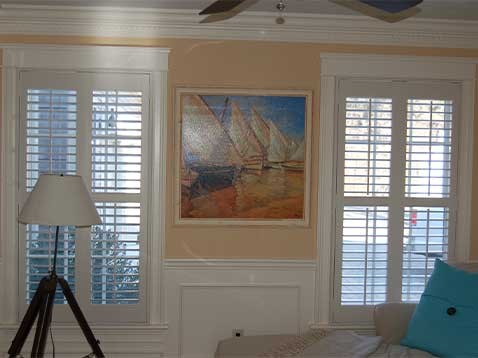 A large painting, bookended by two tall windows covered by shutters